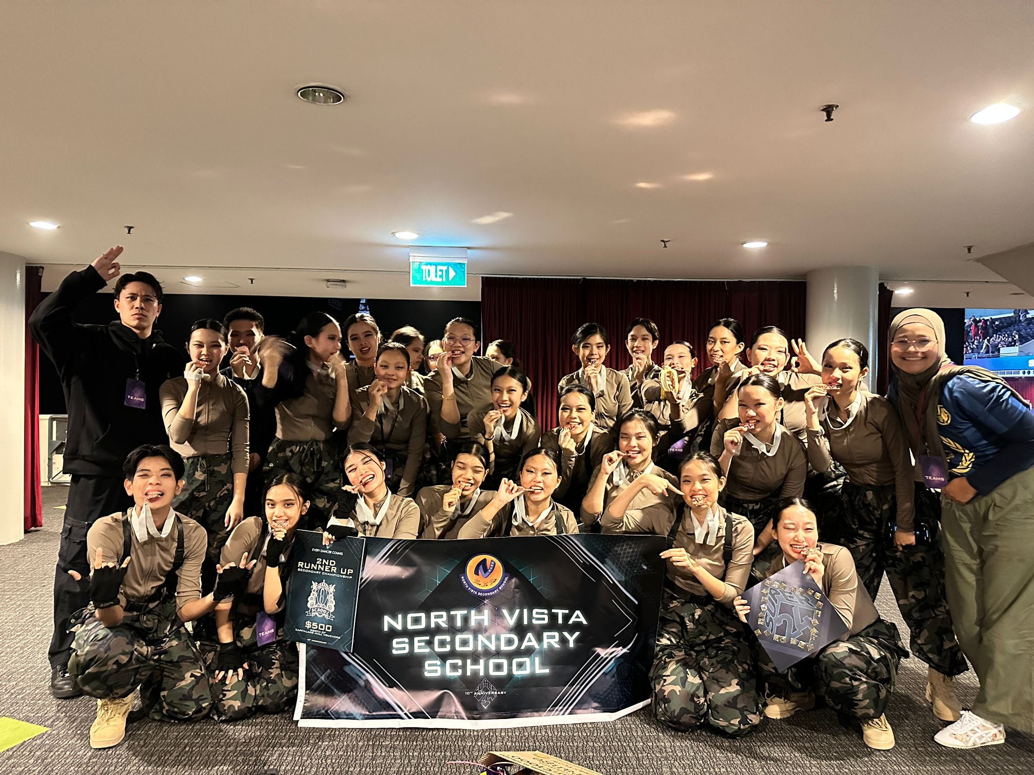 NV modern dancers in camouflage uniforms posing with a North Vista Secondary School banner and 2nd Runner Up award.